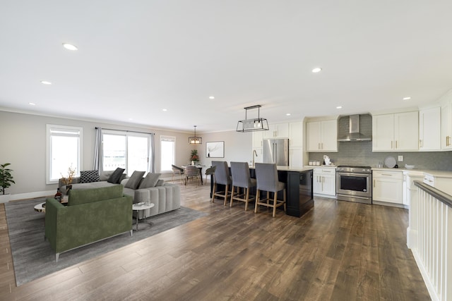 kitchen featuring dark wood-style flooring, open floor plan, light countertops, wall chimney exhaust hood, and appliances with stainless steel finishes