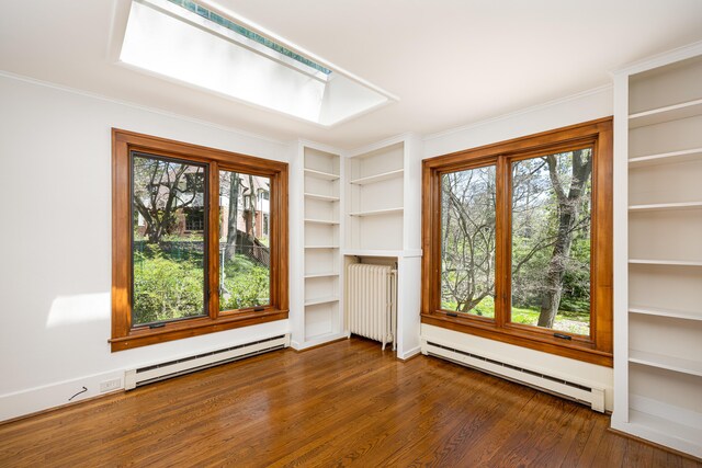 empty room with radiator heating unit, a healthy amount of sunlight, wood finished floors, and a baseboard radiator