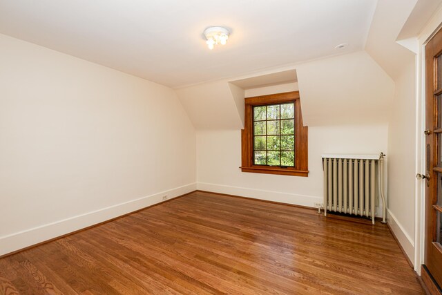 additional living space with baseboards, lofted ceiling, wood finished floors, and radiator