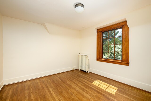 empty room with radiator, baseboards, and wood finished floors