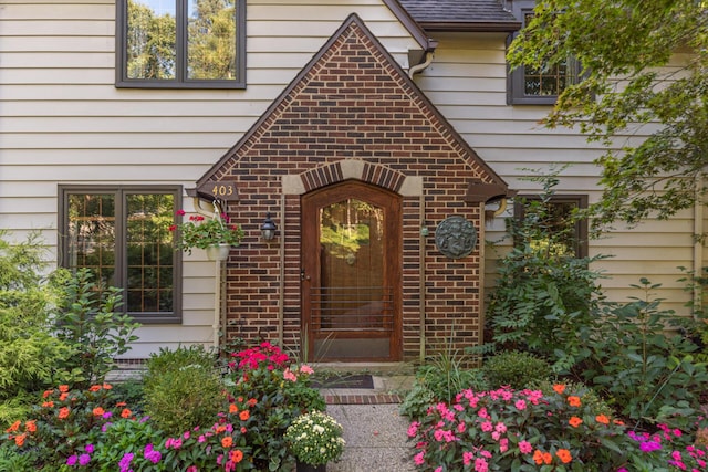 doorway to property featuring brick siding and roof with shingles