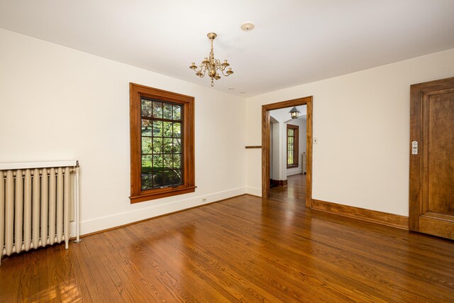 spare room featuring radiator heating unit, baseboards, wood finished floors, and a notable chandelier