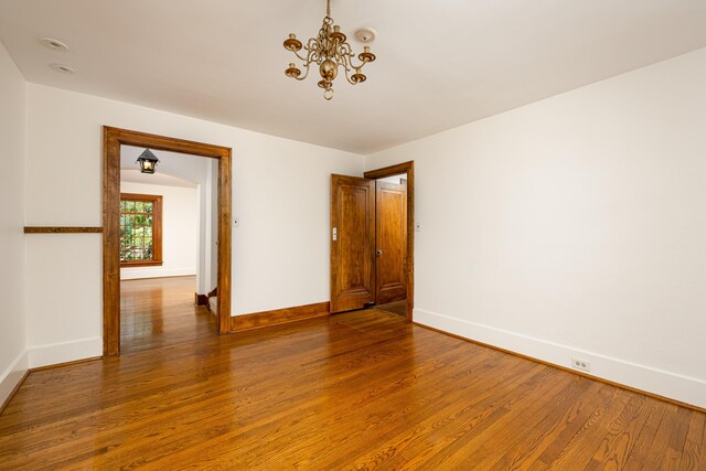spare room featuring baseboards, wood finished floors, and a chandelier