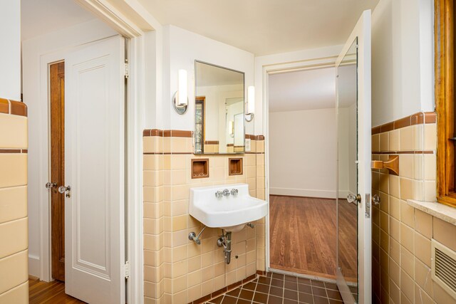 half bath with visible vents, tile walls, wainscoting, wood finished floors, and a sink