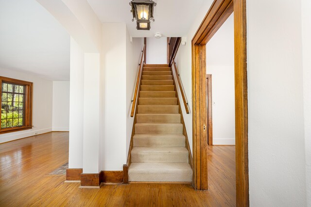 stairs featuring arched walkways, baseboards, and wood finished floors