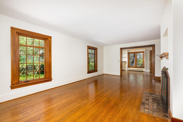 unfurnished room featuring a healthy amount of sunlight, baseboards, a baseboard heating unit, and wood finished floors