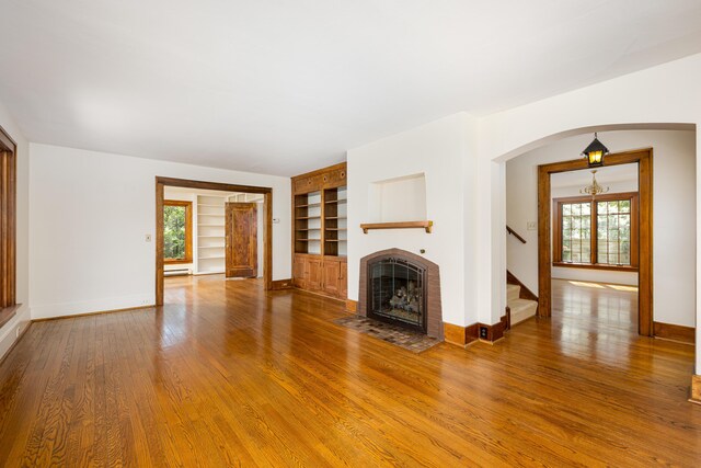 unfurnished living room with built in features, a brick fireplace, wood finished floors, baseboards, and stairs
