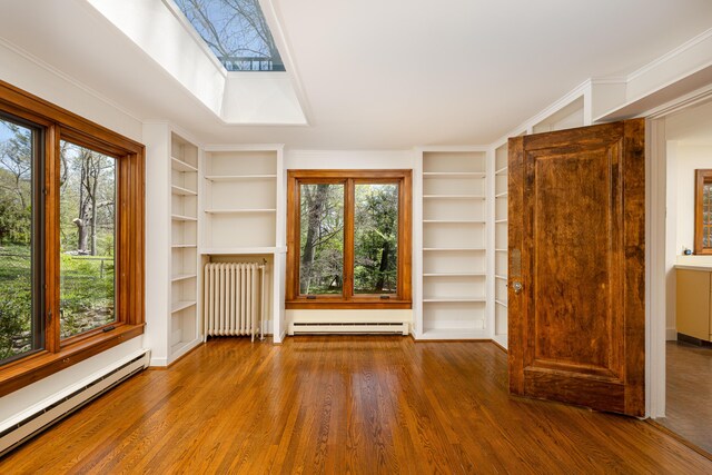 unfurnished living room with a baseboard heating unit, built in shelves, and radiator heating unit