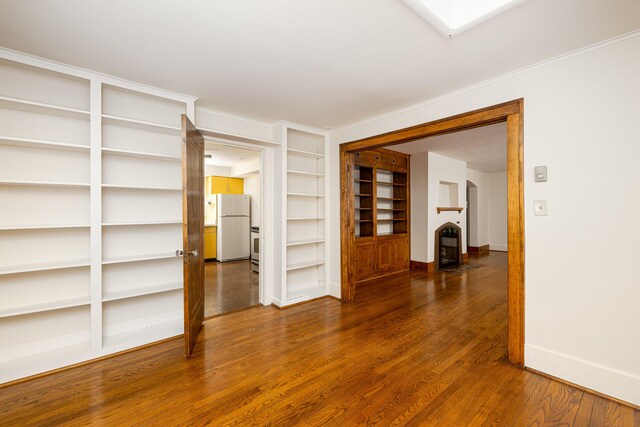 empty room featuring baseboards, built in features, wood finished floors, and a fireplace