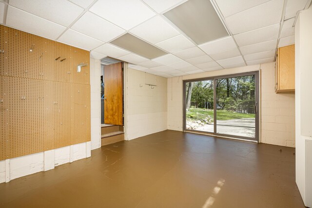 empty room with concrete flooring, concrete block wall, and a drop ceiling