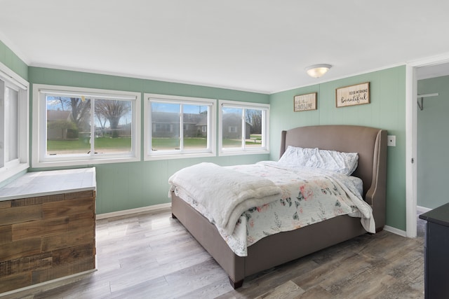 bedroom featuring multiple windows, wood finished floors, baseboards, and crown molding