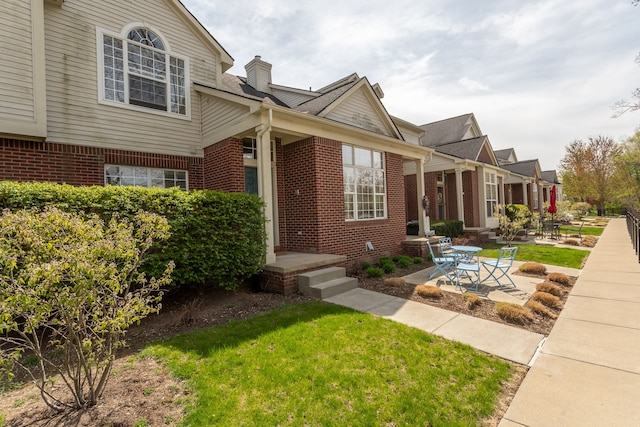 view of front of home featuring a chimney, a front lawn, and brick siding