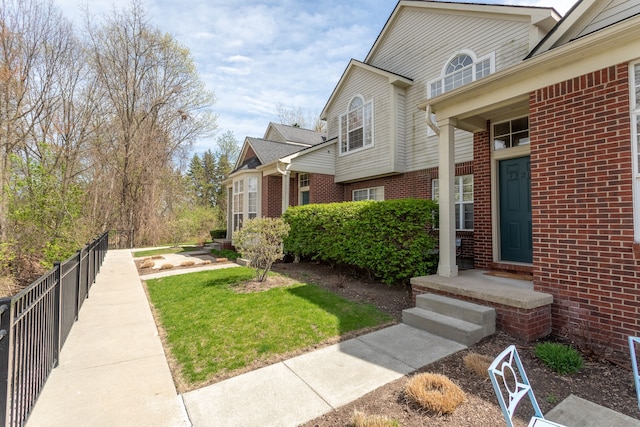view of side of home featuring fence, a yard, and brick siding