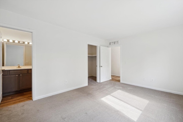 unfurnished bedroom with baseboards, carpet flooring, ensuite bath, visible vents, and a spacious closet