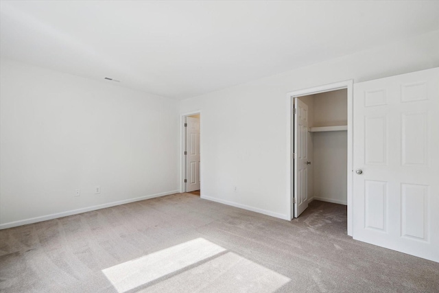 unfurnished bedroom with a walk in closet, carpet, baseboards, and visible vents