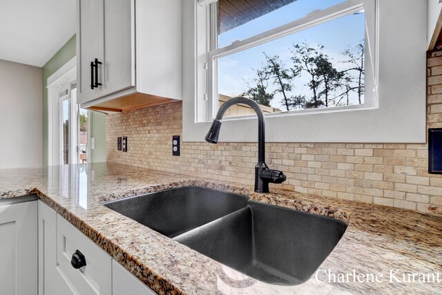 room details featuring light stone counters, a sink, backsplash, and white cabinets