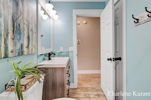 bathroom featuring vanity, toilet, baseboards, wood finished floors, and backsplash