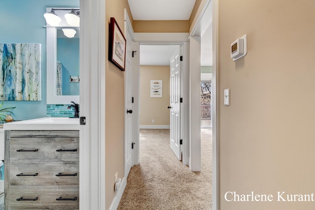 hall featuring baseboards, carpet flooring, and a sink