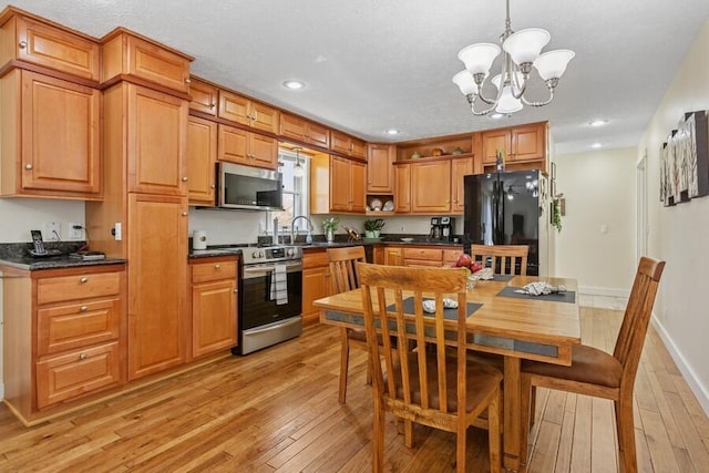 kitchen featuring dark countertops, appliances with stainless steel finishes, a sink, light wood finished floors, and a chandelier