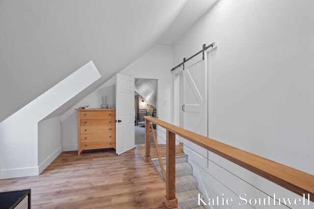 additional living space with baseboards, a barn door, light wood finished floors, and vaulted ceiling with skylight