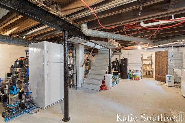 unfinished basement with freestanding refrigerator and stairway