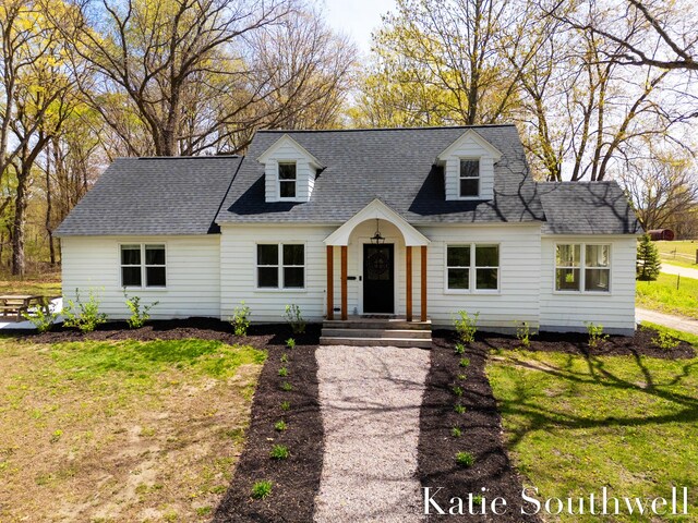new england style home featuring a shingled roof and a front lawn