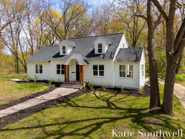 new england style home featuring a shingled roof and a front yard