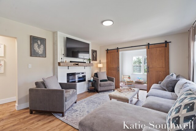 living room featuring a large fireplace, baseboards, a barn door, and light wood-style flooring