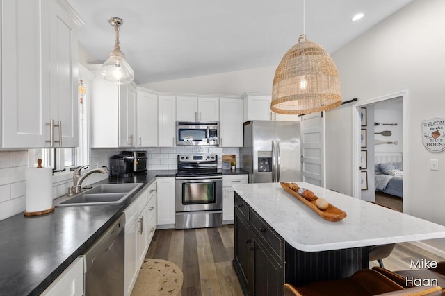 kitchen with appliances with stainless steel finishes, a sink, white cabinetry, tasteful backsplash, and vaulted ceiling
