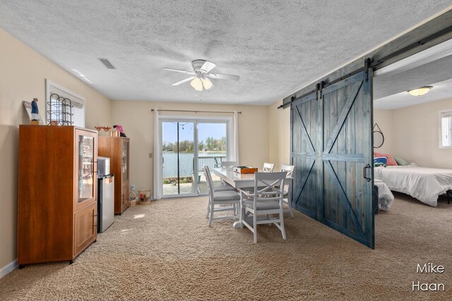 dining space with a water view, ceiling fan, a barn door, and light colored carpet