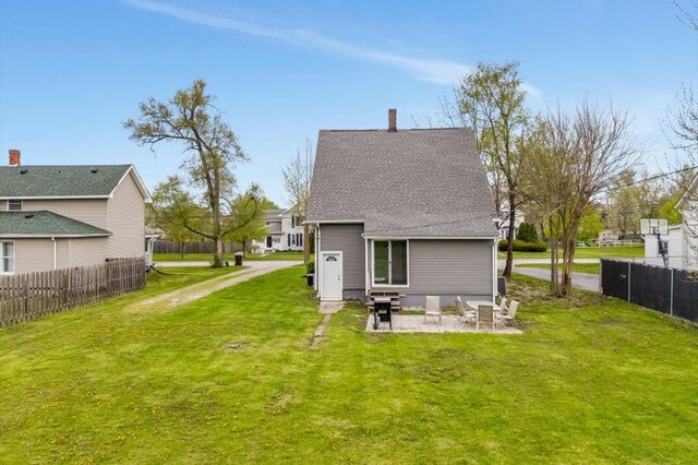 back of house with fence, a shingled roof, a chimney, a patio, and a yard