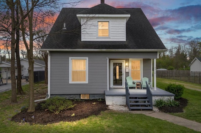 back of house with fence, covered porch, a shingled roof, and a yard