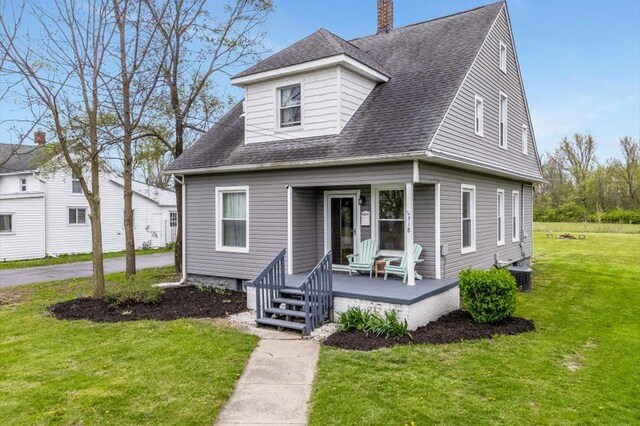 view of front of house with roof with shingles, covered porch, a chimney, and a front yard
