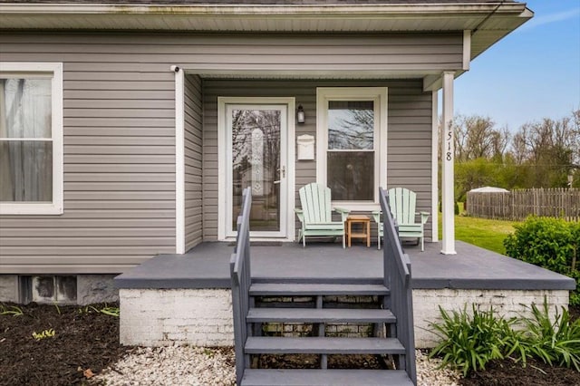 view of exterior entry featuring fence and a porch