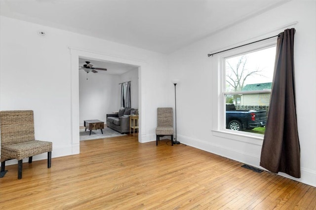 sitting room featuring visible vents, a ceiling fan, light wood-style floors, and baseboards
