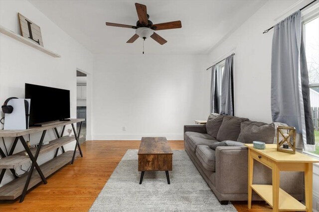 living room with a ceiling fan, baseboards, and light wood-style flooring