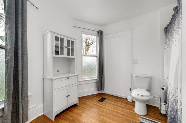 bathroom featuring baseboards, toilet, wood finished floors, and visible vents