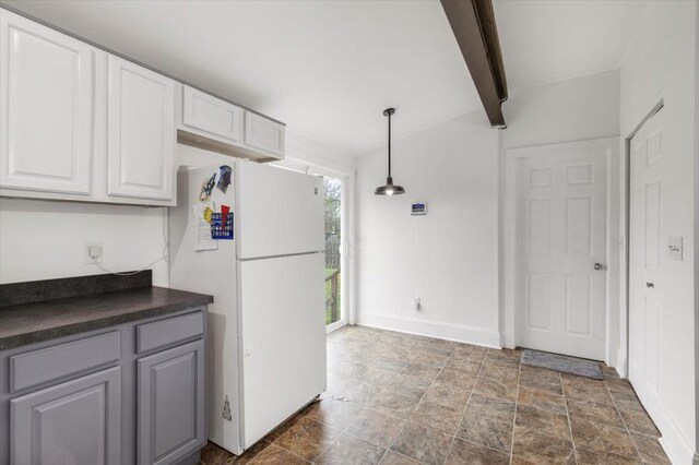 kitchen with freestanding refrigerator, dark countertops, gray cabinets, white cabinetry, and stone finish flooring