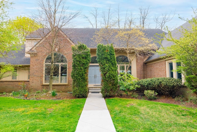 ranch-style house featuring roof with shingles, a front lawn, and brick siding