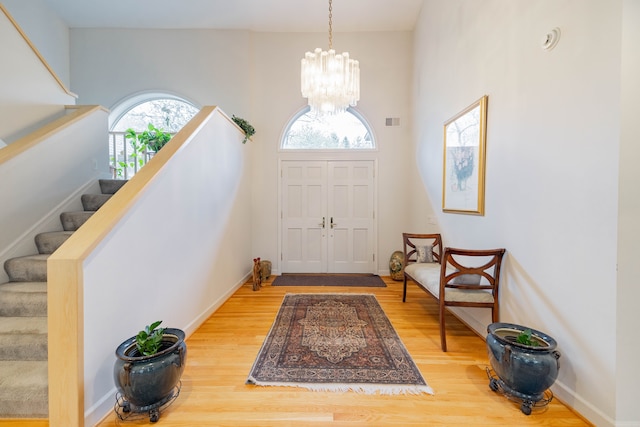 foyer entrance with visible vents, an inviting chandelier, wood finished floors, and stairway