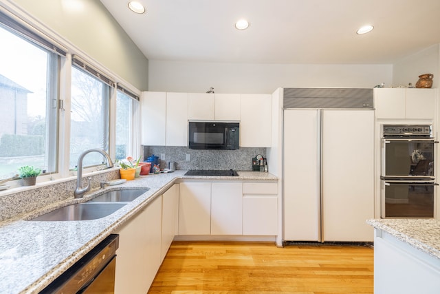 kitchen with backsplash, a sink, black appliances, light wood-style floors, and white cabinetry