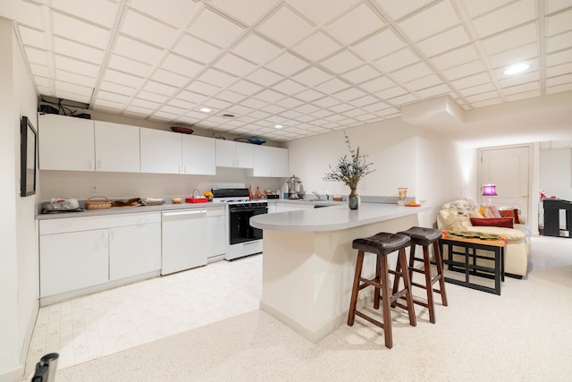 kitchen featuring a peninsula, white appliances, a breakfast bar, white cabinets, and a sink
