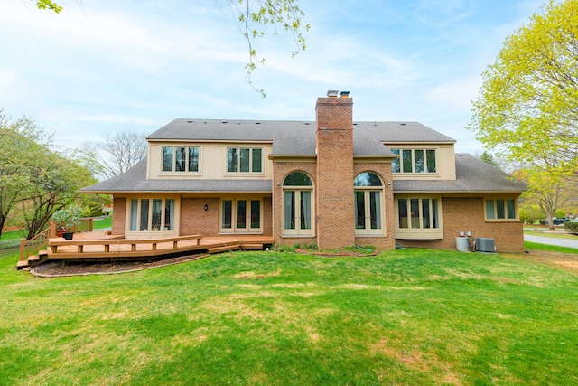 rear view of property with brick siding, a yard, a chimney, and a deck