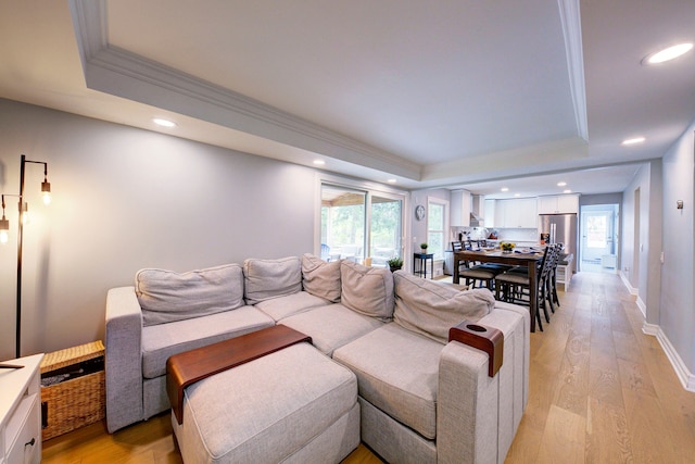 living room featuring a tray ceiling, light wood-style floors, ornamental molding, and recessed lighting