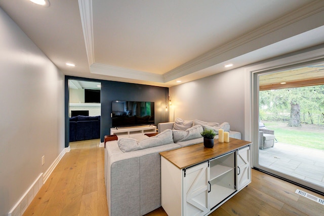 living area featuring crown molding, a raised ceiling, light wood finished floors, and visible vents