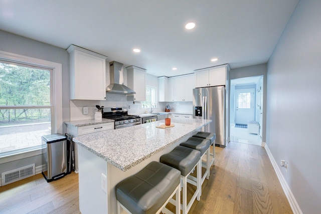 kitchen featuring a sink, stainless steel appliances, visible vents, wall chimney exhaust hood, and light wood-style flooring