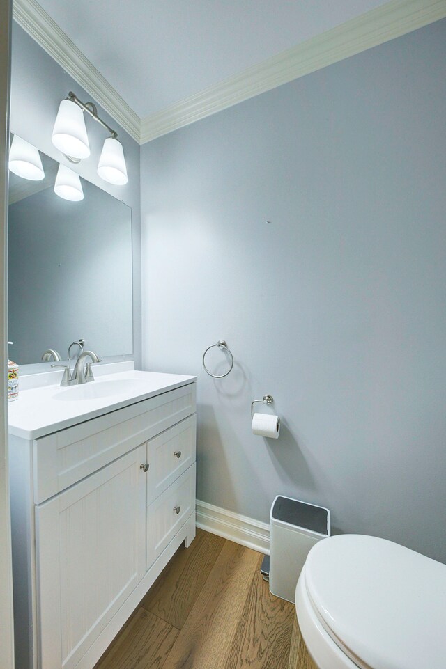 half bath featuring toilet, wood finished floors, vanity, ornamental molding, and baseboards