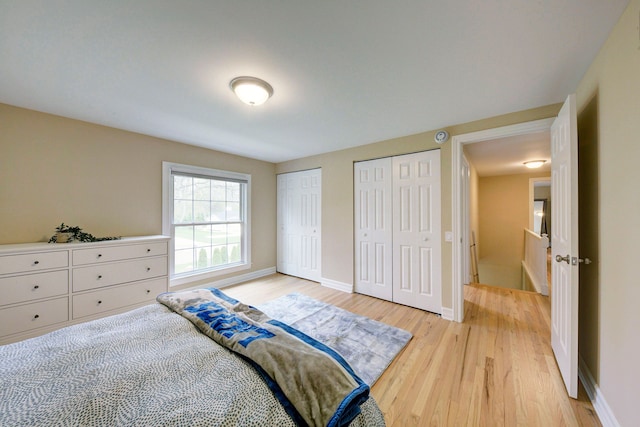 bedroom featuring two closets, light wood-style flooring, and baseboards