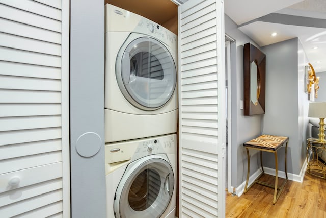 clothes washing area featuring laundry area, baseboards, stacked washing maching and dryer, recessed lighting, and light wood finished floors