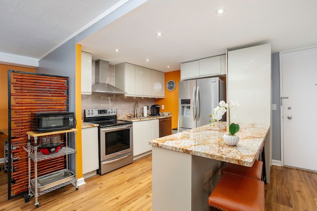 kitchen featuring a sink, appliances with stainless steel finishes, light wood-style flooring, and wall chimney exhaust hood